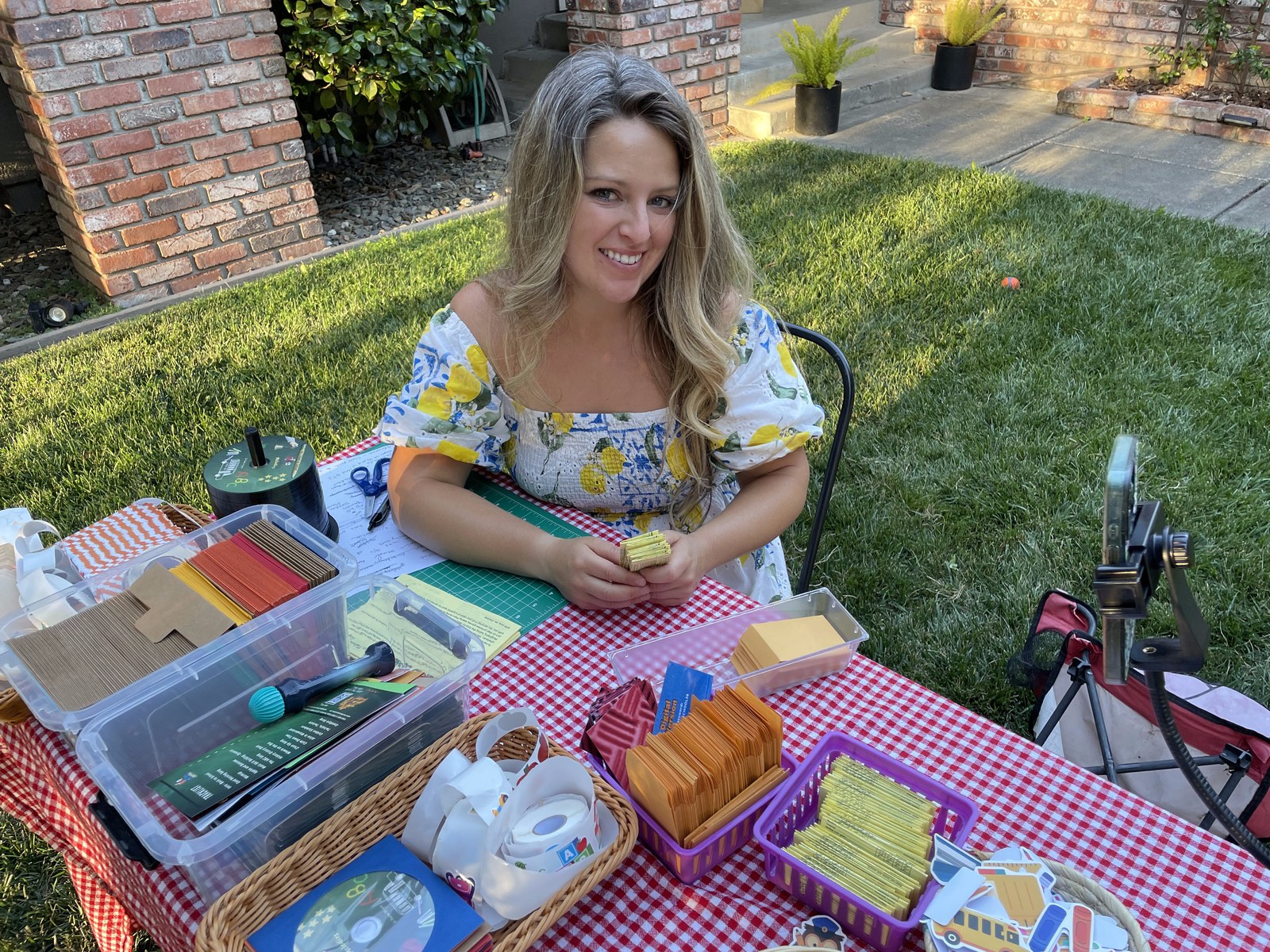Chelsea at a table outdoors packing Mailbox Melodies envelopes, surrounded by stickers, cards and CDs