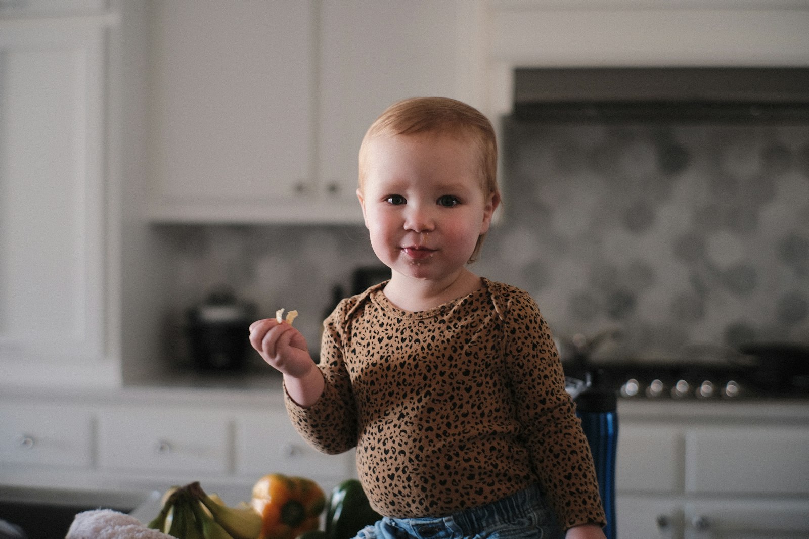 A toddler dancing in the kitchen with hands in the air
