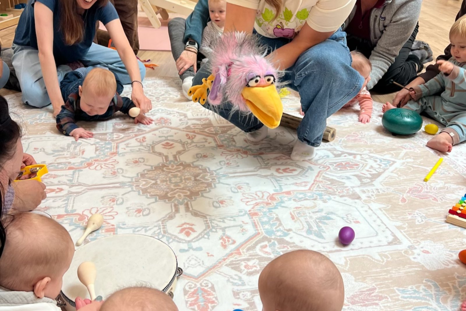 Babies at a music class sitting on a rug with shakers and small cymbals