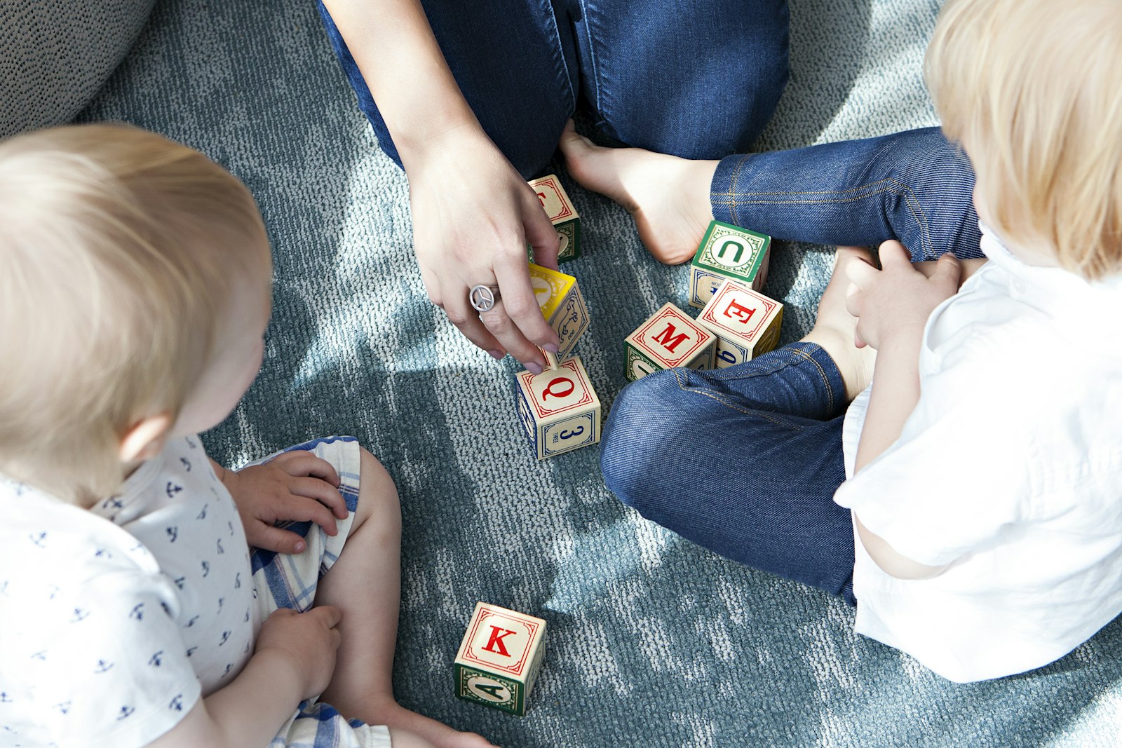 Two toddlers and a parent playing with wooden letter blocks on a rug, screen free activities for kids