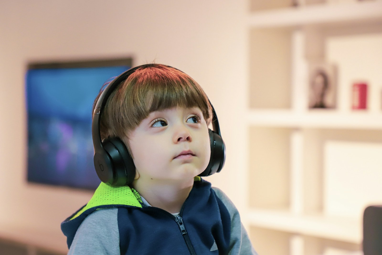 A child listening with headphones beside a shelf at home, using one of the best music subscriptions for kids