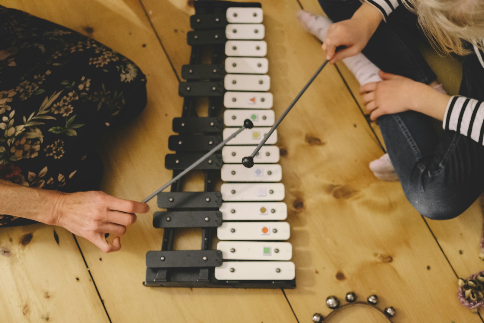 An adult and a toddler playing a wooden xylophone together on the floor