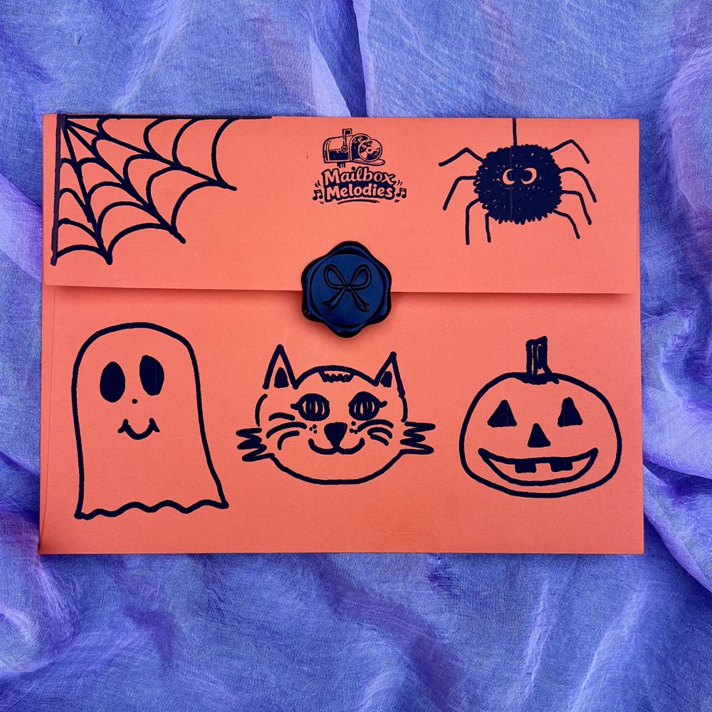 The orange Halloween Mailbox Melodies envelope with ghost, cat and pumpkin drawings