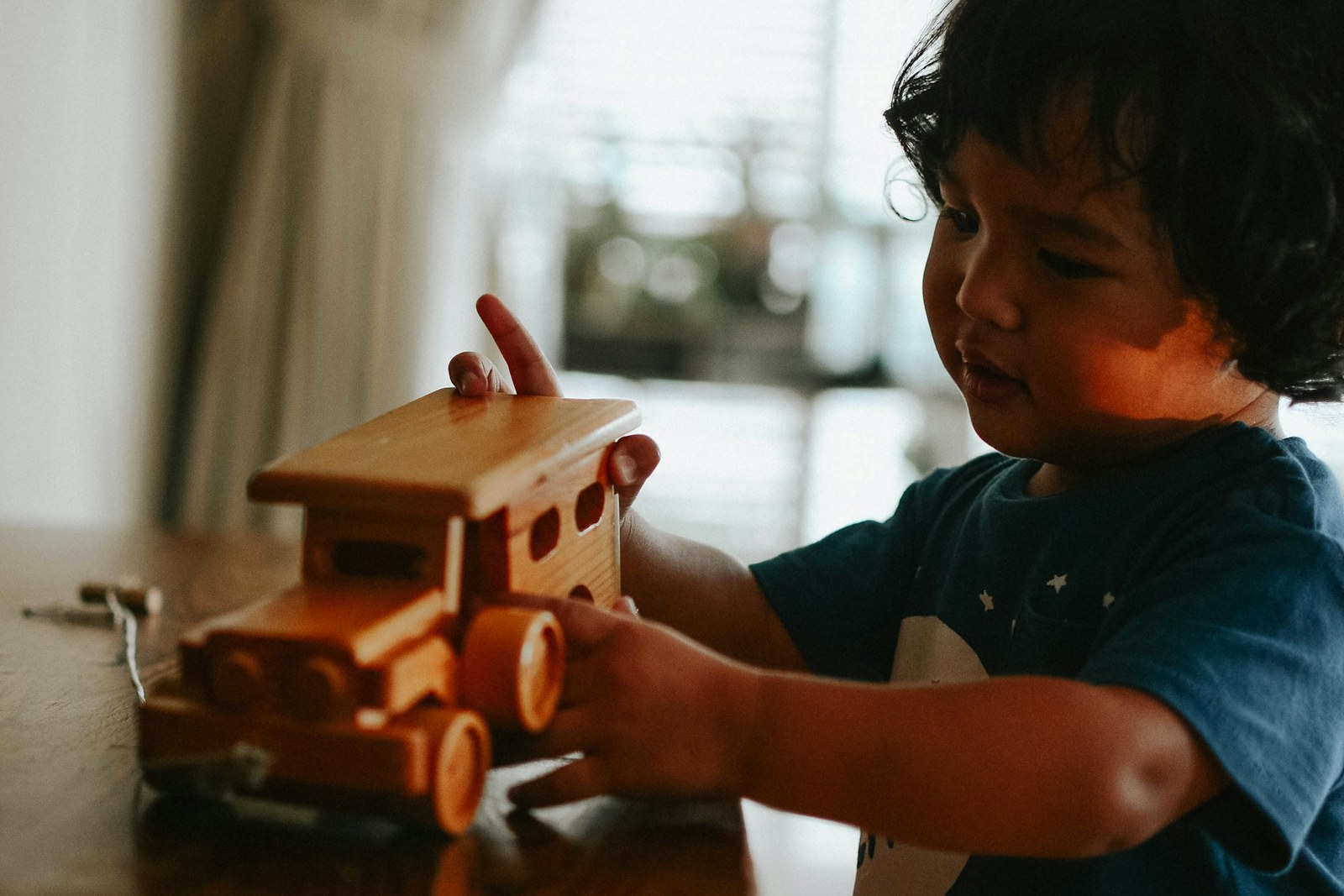 A toddler playing with a wooden toy truck on the floor