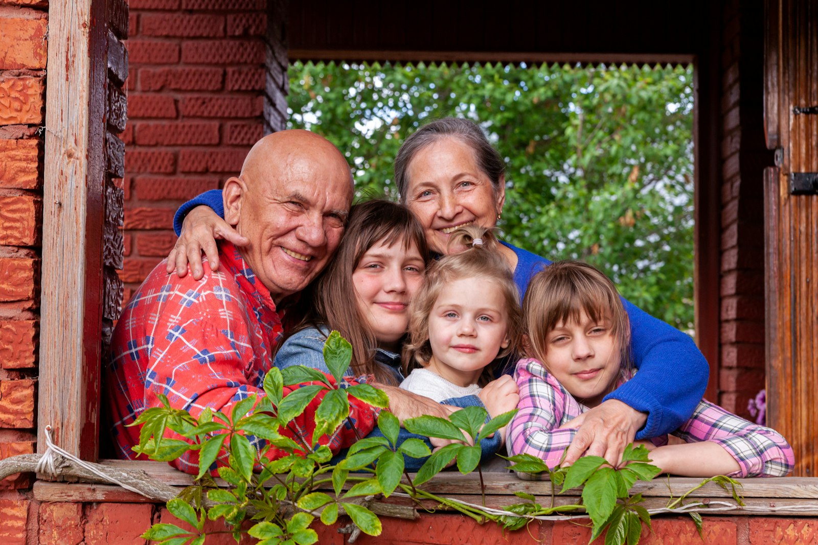 Grandparents hugging their three grandchildren through an open window